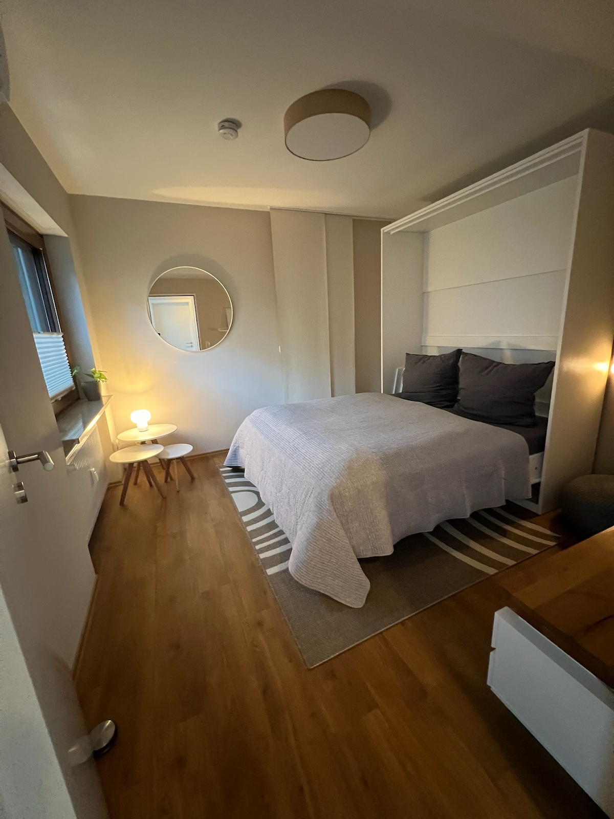 Gemütliches Schlafzimmer im Goodie Room Apartment mit Doppelbett, warmem Licht, Spiegel und natürlicher Einrichtung